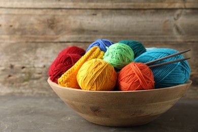 Different yarns, knitting needles and pattern sample in bowl on grey table, closeup