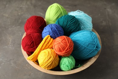 Photo of Different yarns and knitting sample in bowl on grey textured table