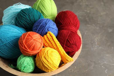 Photo of Different yarns and knitting sample in bowl on grey textured table, closeup