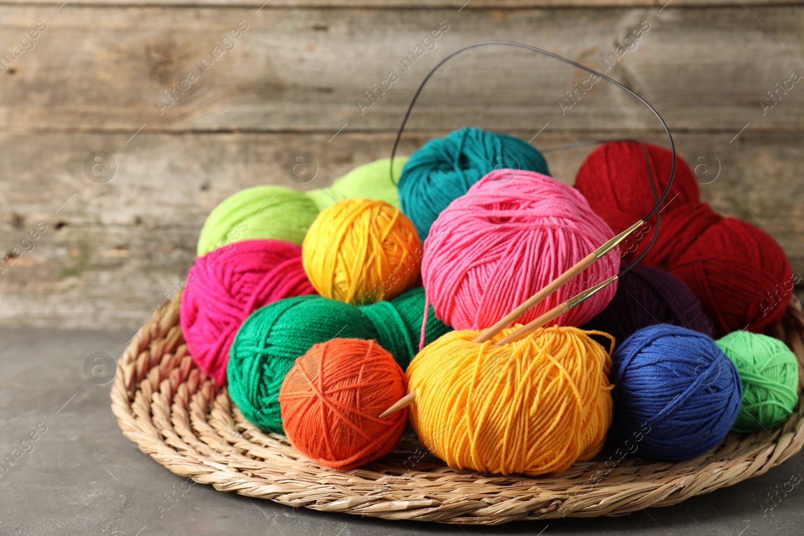 Photo of Pile of different yarns, knitting needles and wicker mat on grey table