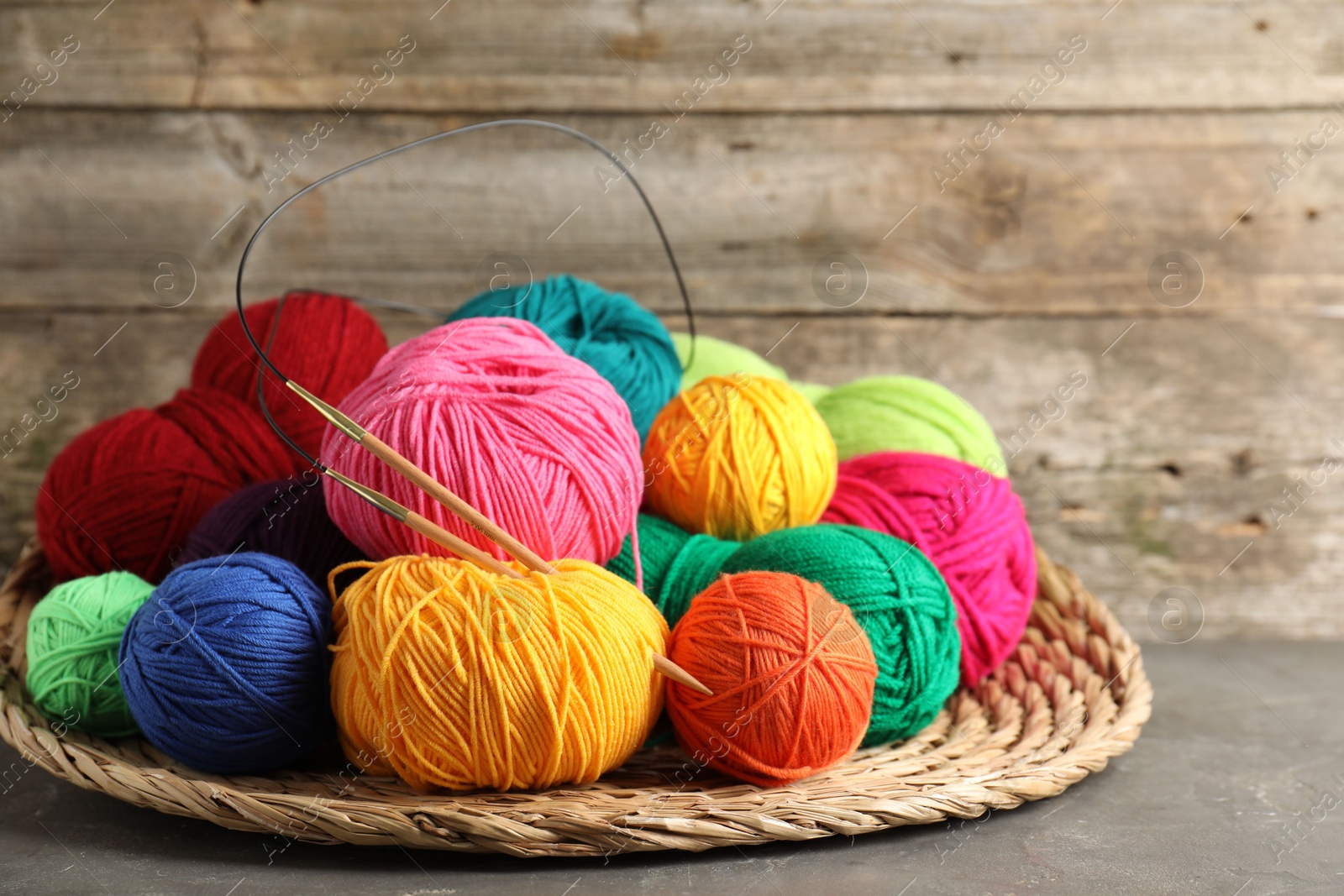 Photo of Pile of different yarns, knitting needles and wicker mat on grey table