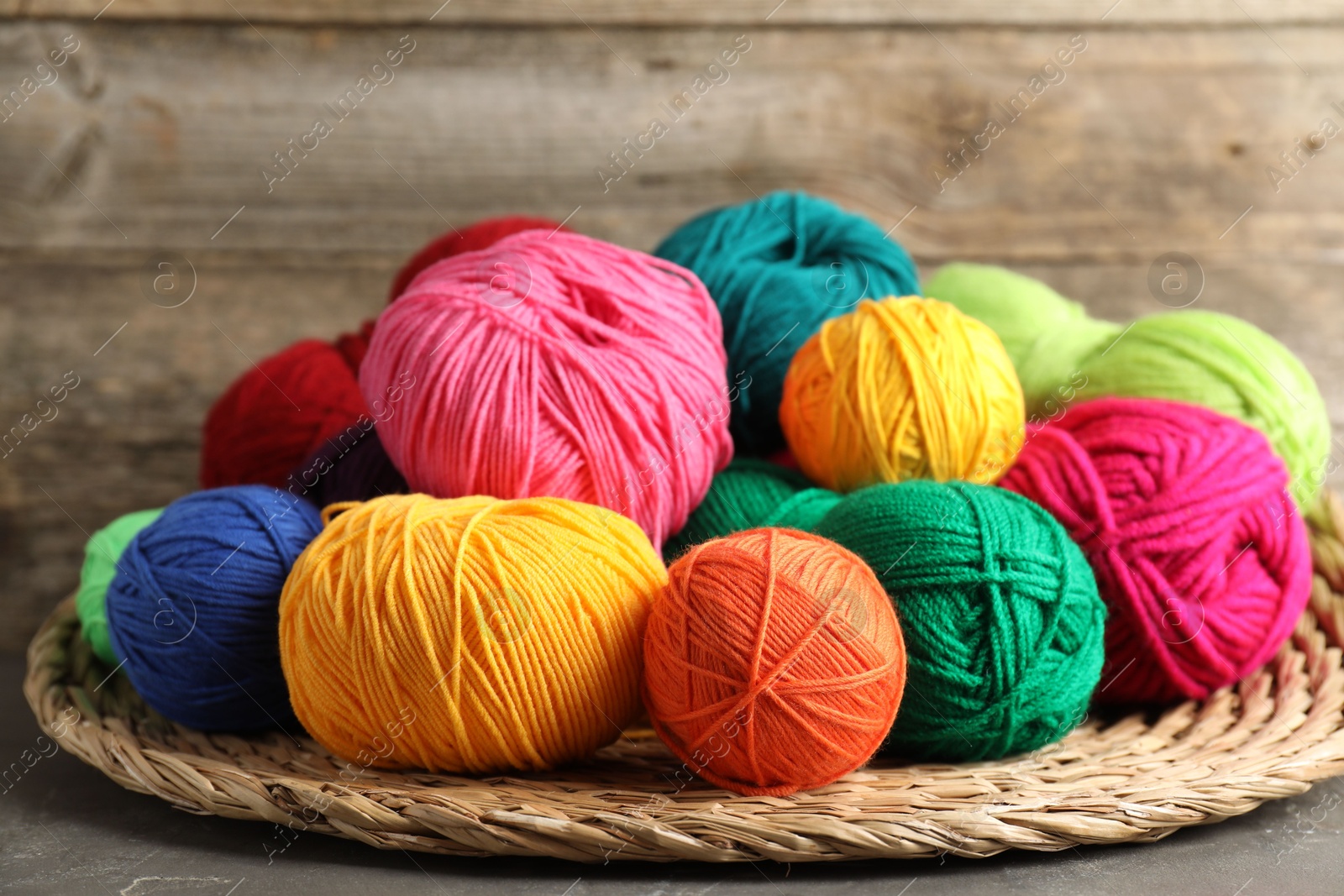 Photo of Pile of different yarns, knitting needles and wicker mat on grey table, closeup