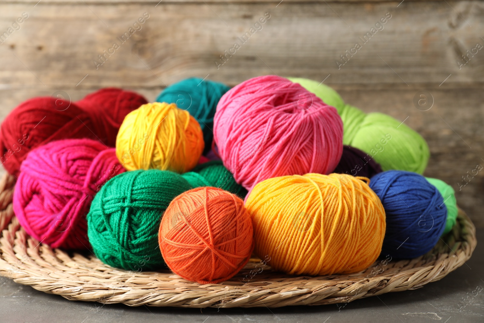 Photo of Pile of different yarns, knitting needles and wicker mat on grey table, closeup