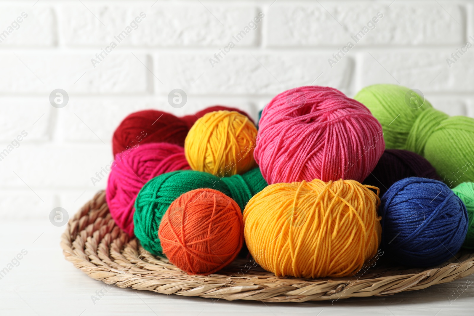 Photo of Pile of different yarns and wicker mat on white wooden table, closeup