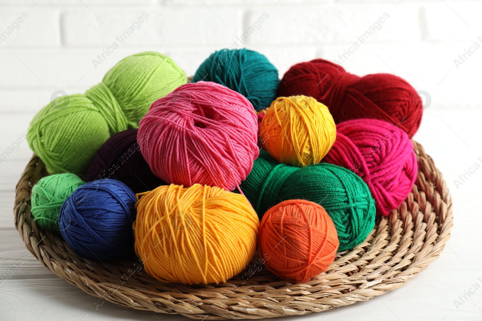 Photo of Pile of different yarns and wicker mat on white wooden table, closeup