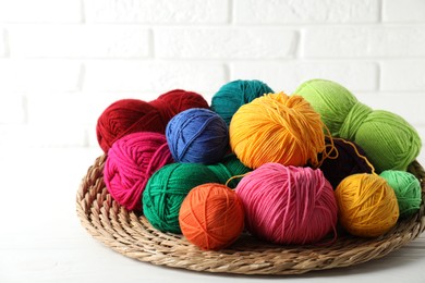 Photo of Pile of different yarns and wicker mat on white wooden table, closeup