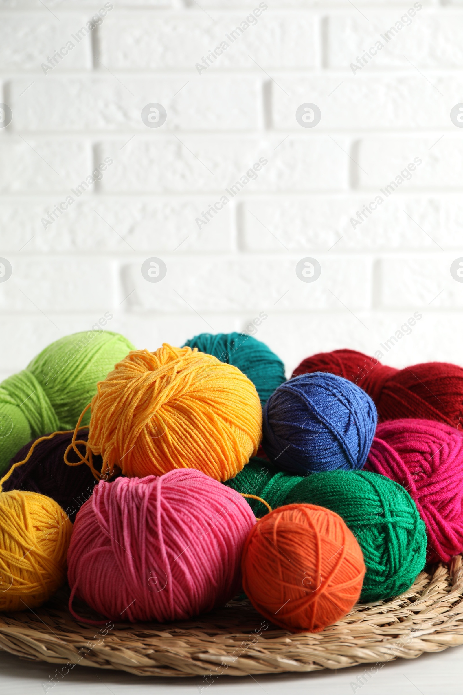 Photo of Pile of different yarns and wicker mat on white table against brick wall. Space for text