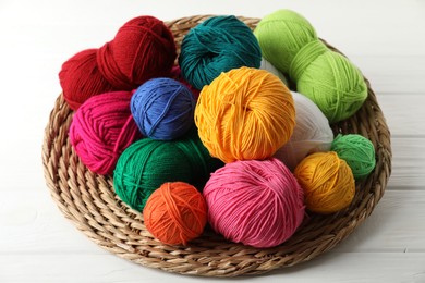 Photo of Pile of different yarns and wicker mat on white wooden table