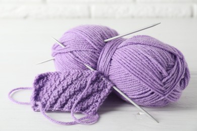 Photo of Skein of yarn, knitting needles and pattern sample on white wooden table, closeup