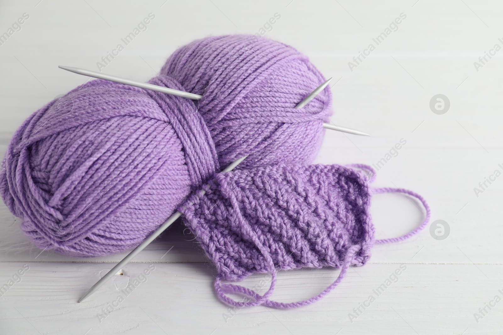 Photo of Skein of yarn, knitting needles and pattern sample on white wooden table, closeup