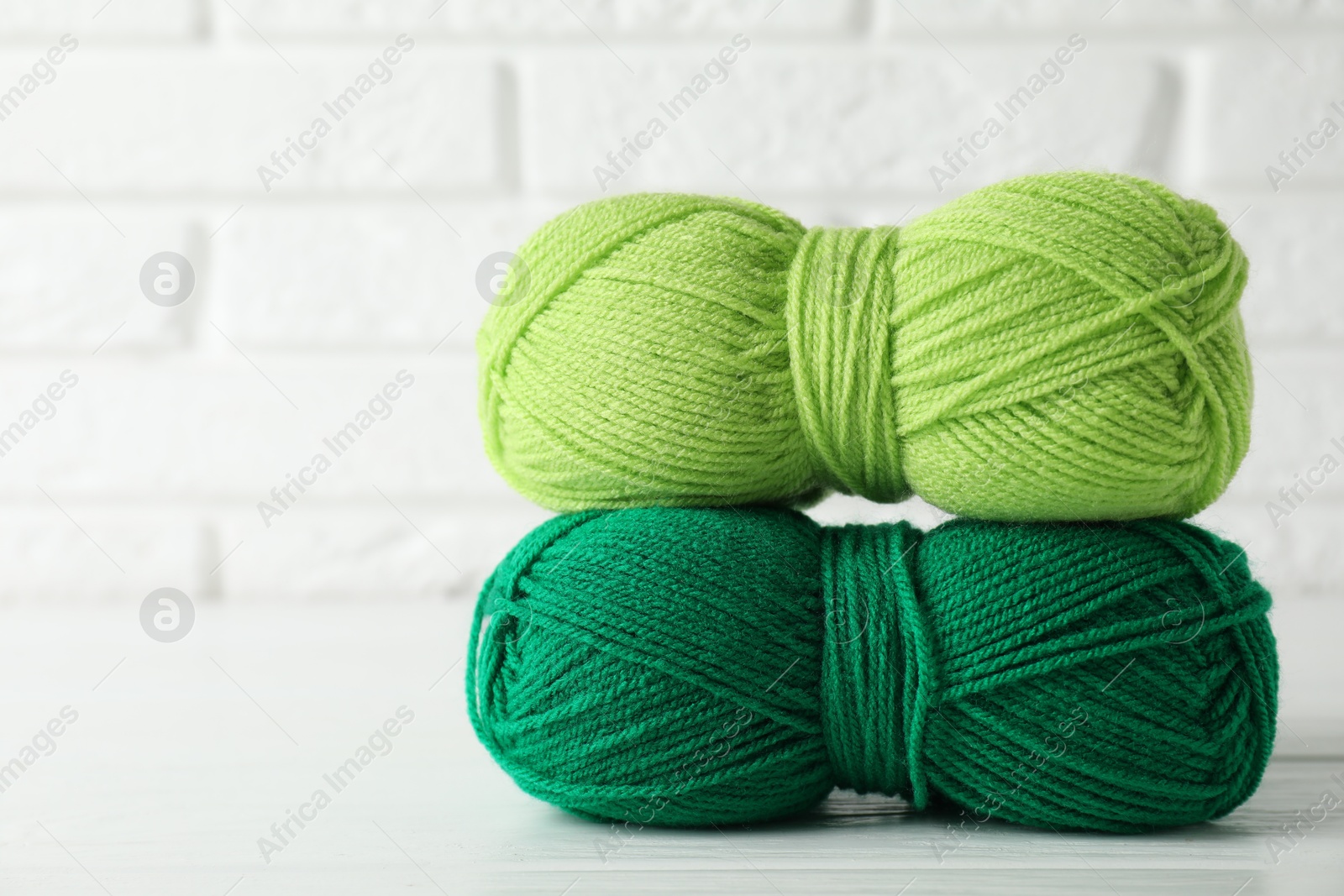 Photo of Skeins of colorful yarns on white wooden table against brick wall, closeup. Space for text