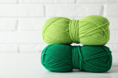 Photo of Skeins of colorful yarns on white wooden table against brick wall, closeup. Space for text