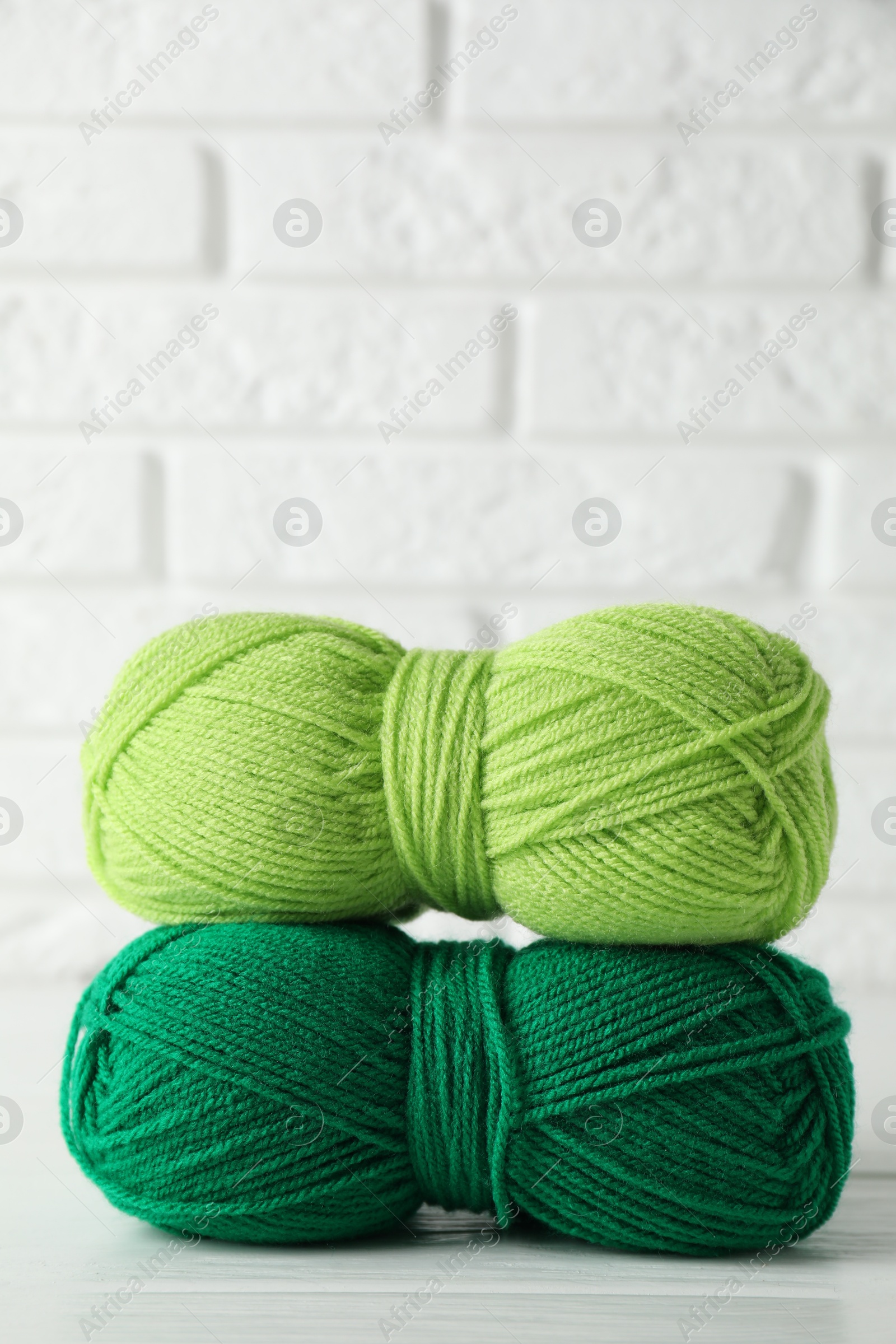 Photo of Skeins of colorful yarns on white wooden table against brick wall