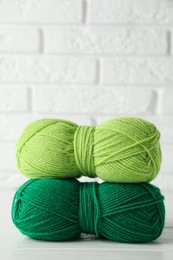 Skeins of colorful yarns on white wooden table against brick wall