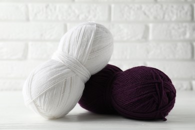 Photo of Skeins of colorful yarns on white wooden table against brick wall, closeup