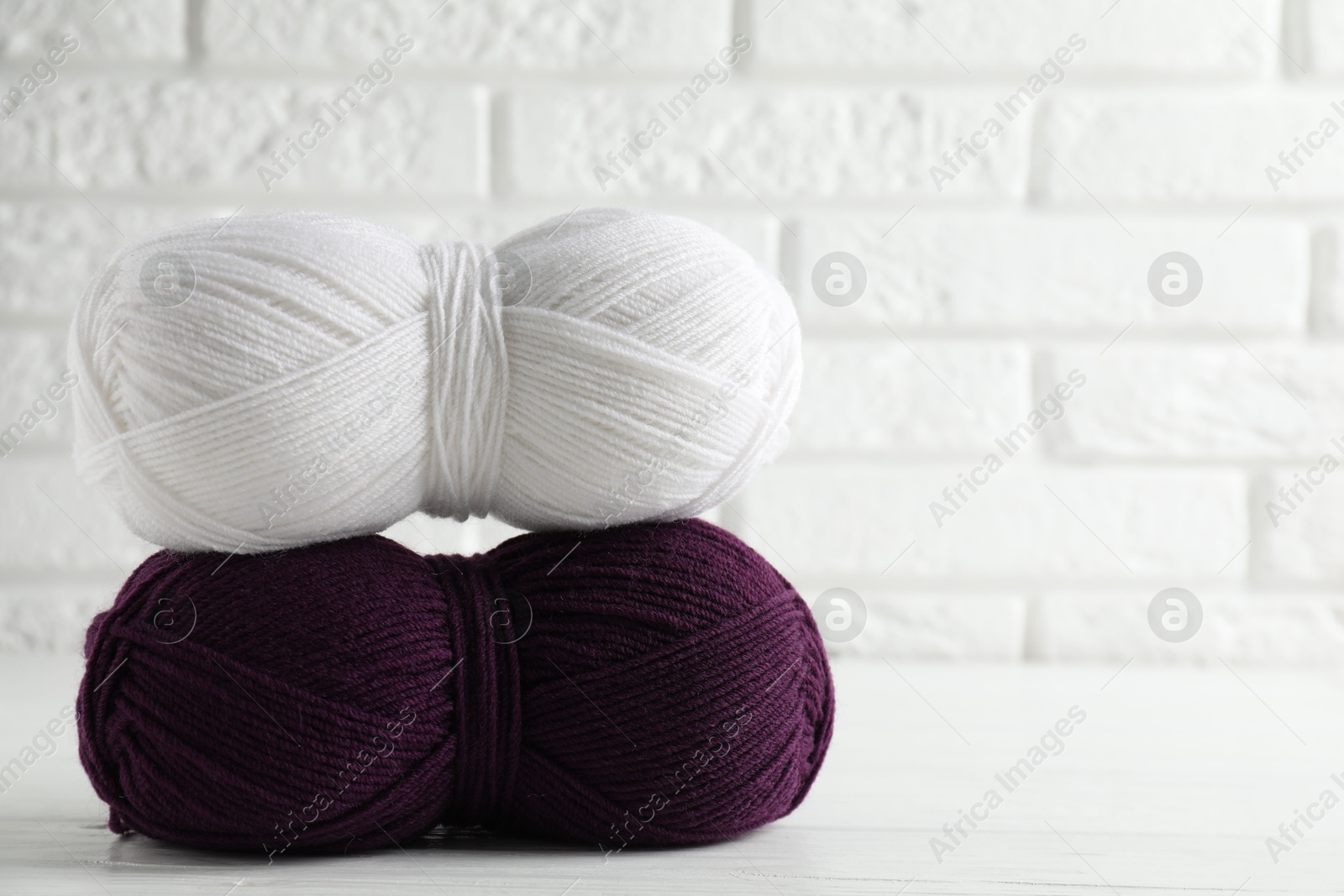 Photo of Skeins of colorful yarns on white wooden table against brick wall, closeup. Space for text