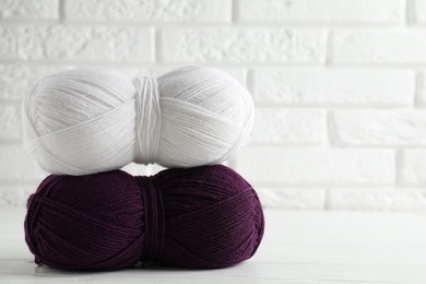 Photo of Skeins of colorful yarns on white wooden table against brick wall, closeup. Space for text