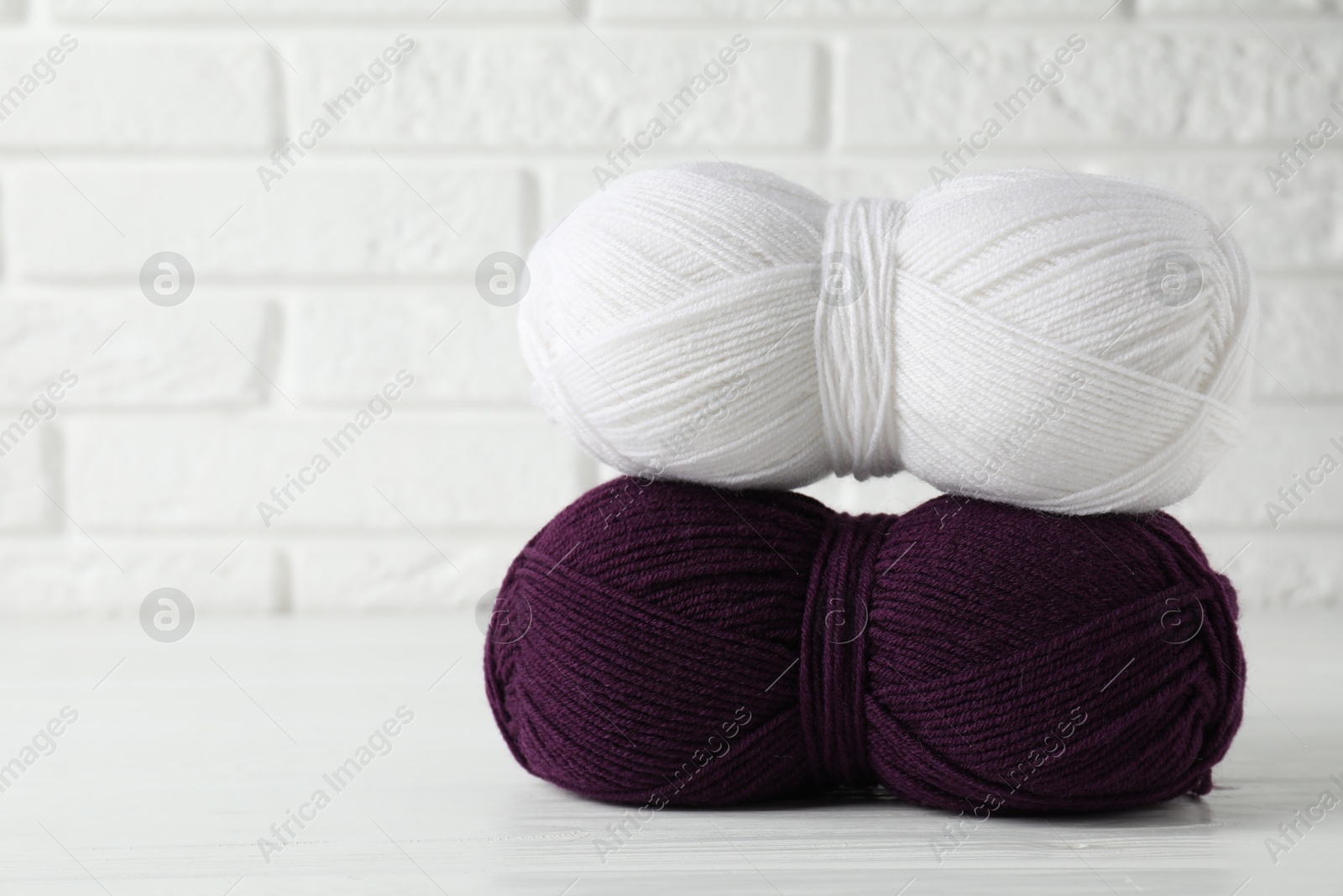 Photo of Skeins of colorful yarns on white wooden table against brick wall, closeup. Space for text