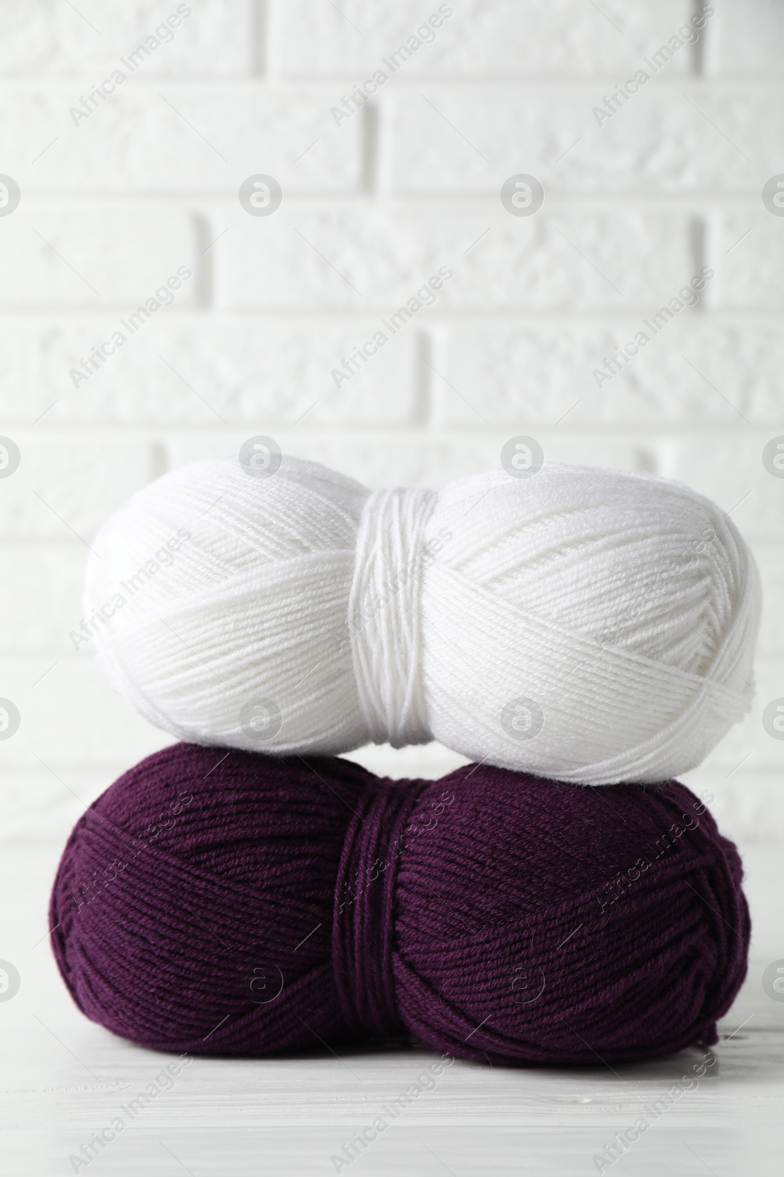 Photo of Skeins of colorful yarns on white wooden table against brick wall