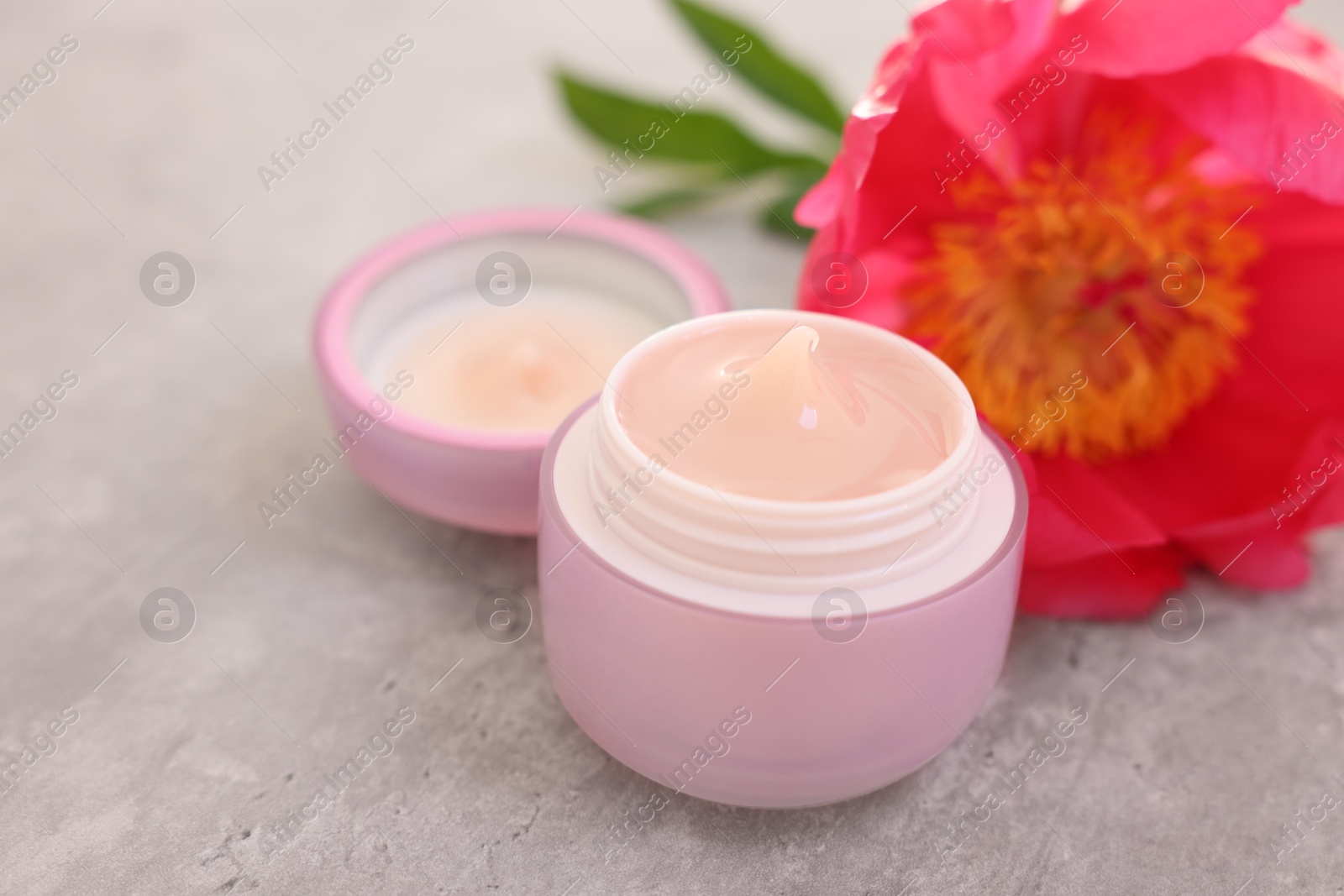 Photo of Jar of cream and peony flower on gray table, closeup