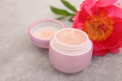 Photo of Jar of cream and peony flower on gray table, closeup