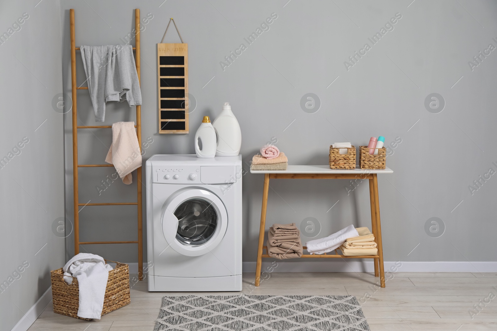 Photo of Washing machine, ladder, detergents, basket, laundry and storage bench indoors