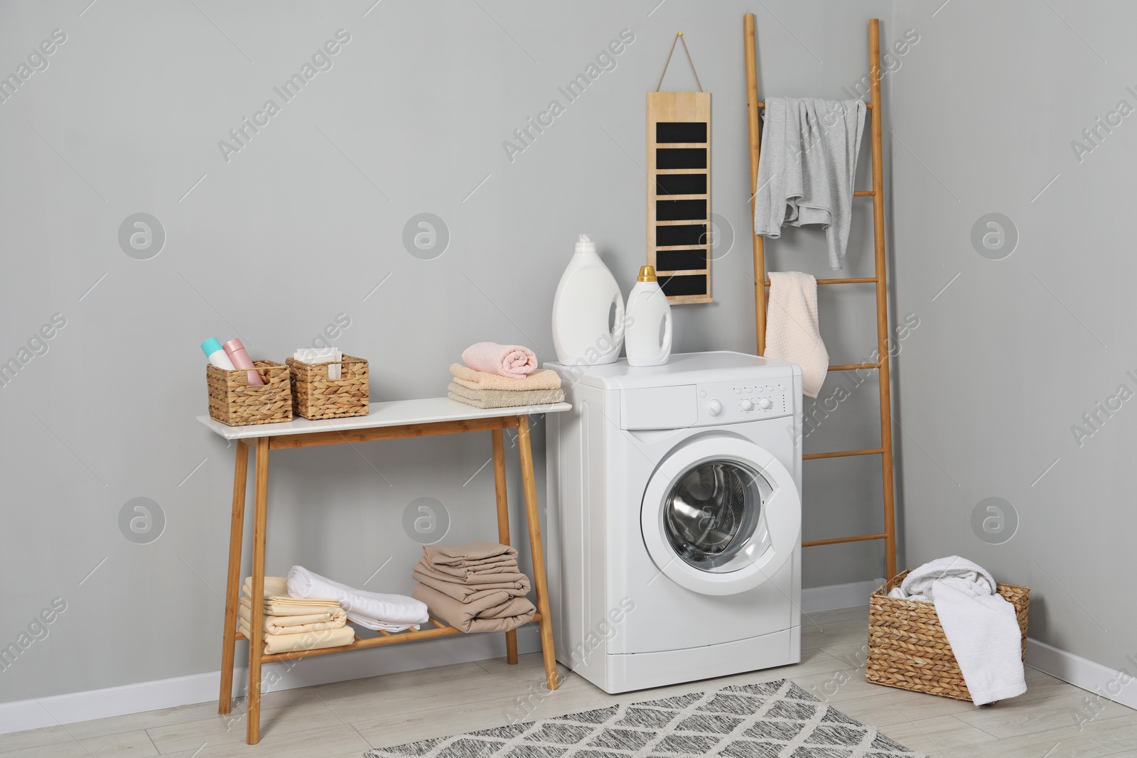 Photo of Washing machine, ladder, detergents, basket, laundry and storage bench indoors