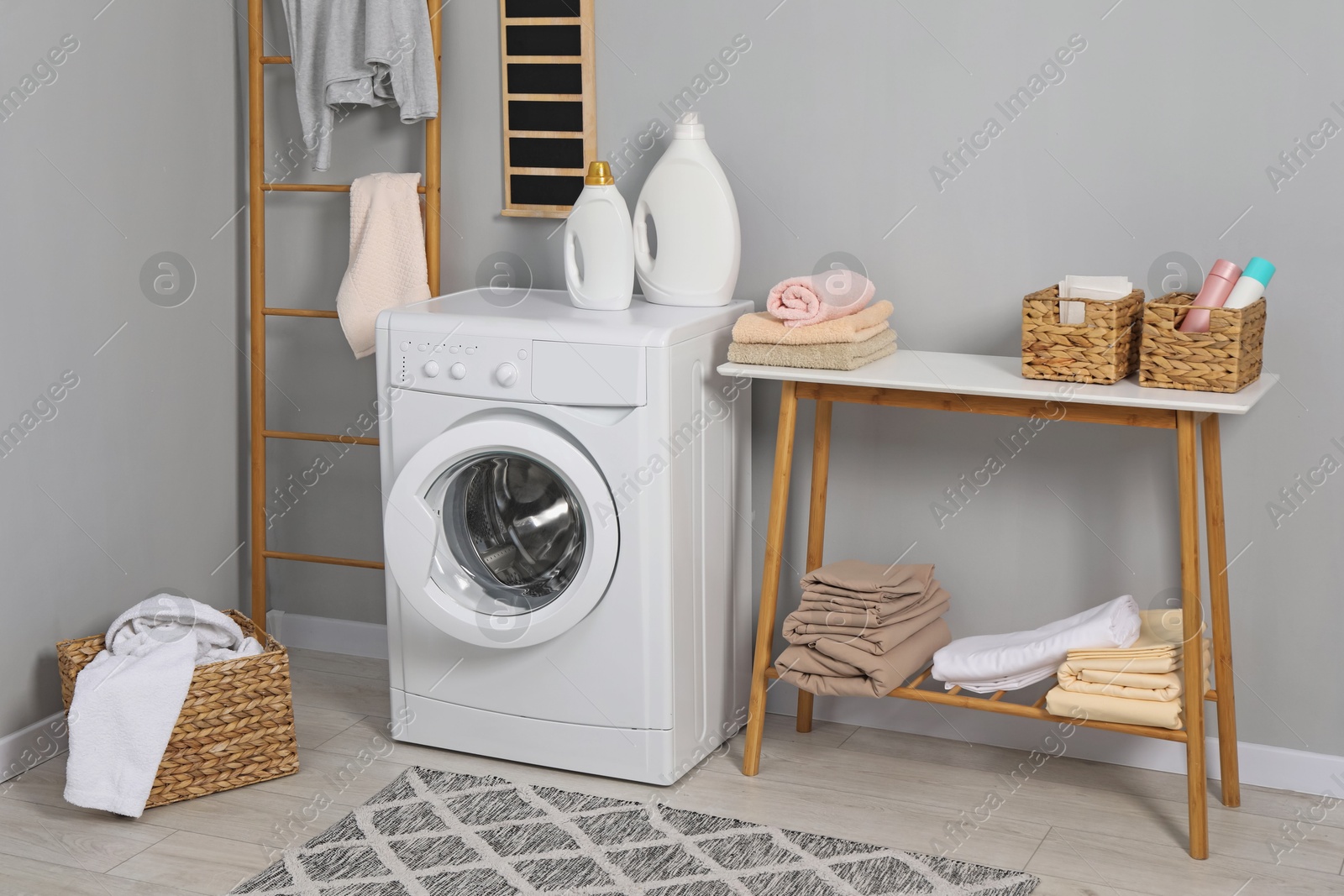 Photo of Washing machine, ladder, detergents, basket, laundry and storage bench indoors