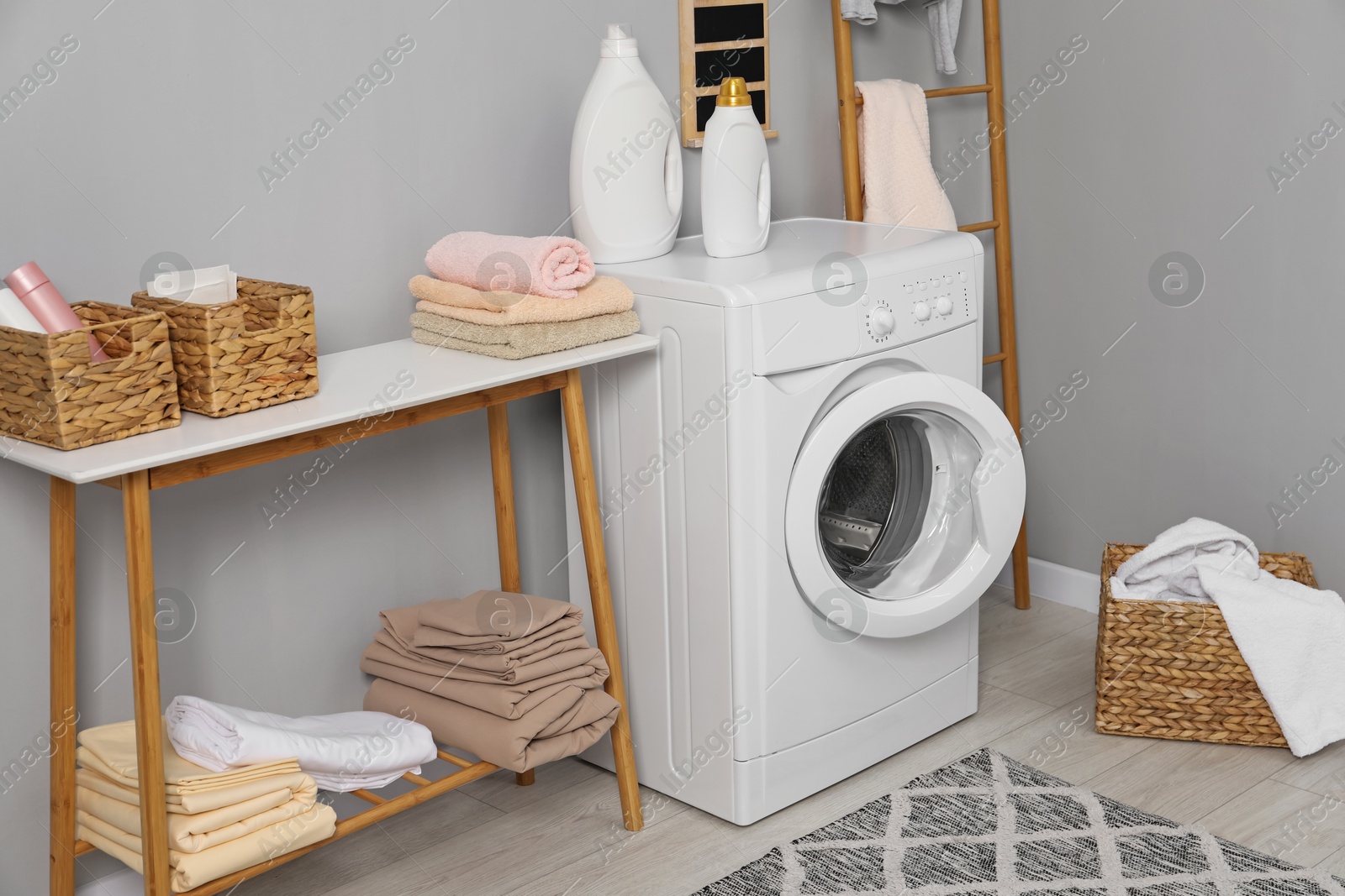 Photo of Washing machine, ladder, detergents, basket, laundry and storage bench indoors