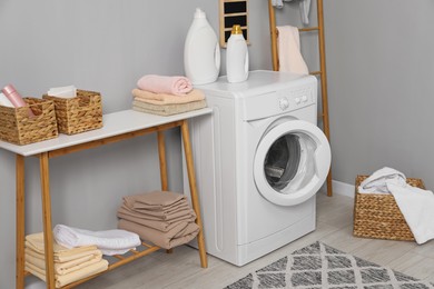 Photo of Washing machine, ladder, detergents, basket, laundry and storage bench indoors