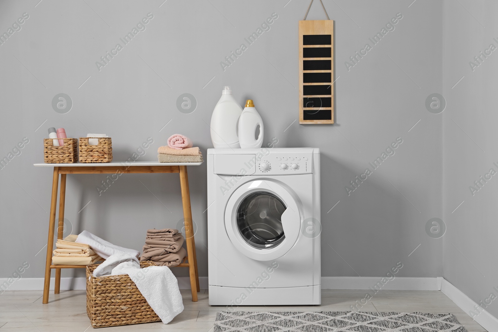 Photo of Washing machine, detergents, basket with laundry and storage bench indoors