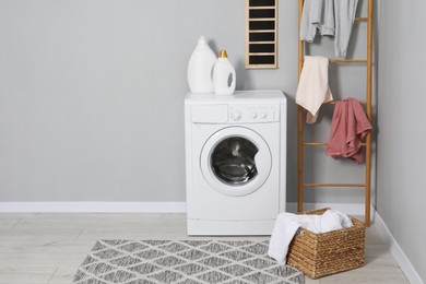 Photo of Washing machine, detergents, ladder, basket and laundry near grey wall indoors, space for text