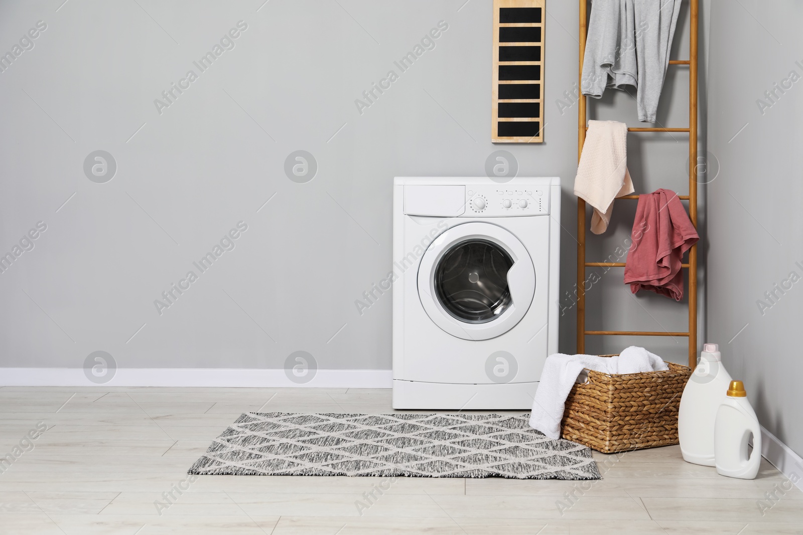 Photo of Washing machine, detergents, ladder, basket and laundry near grey wall indoors, space for text