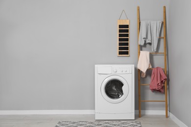 Photo of Washing machine, ladder and laundry near grey wall indoors, space for text