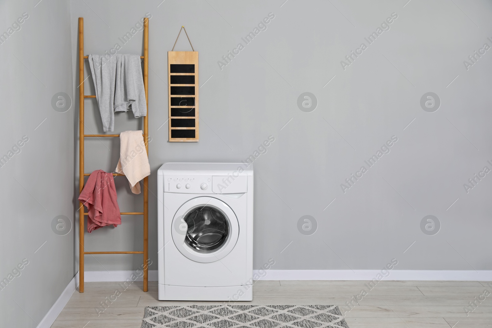 Photo of Washing machine, ladder and laundry near grey wall indoors, space for text