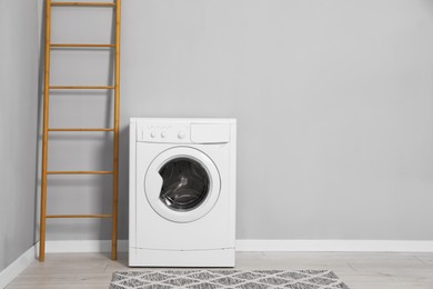 Photo of Washing machine and ladder near grey wall indoors, space for text