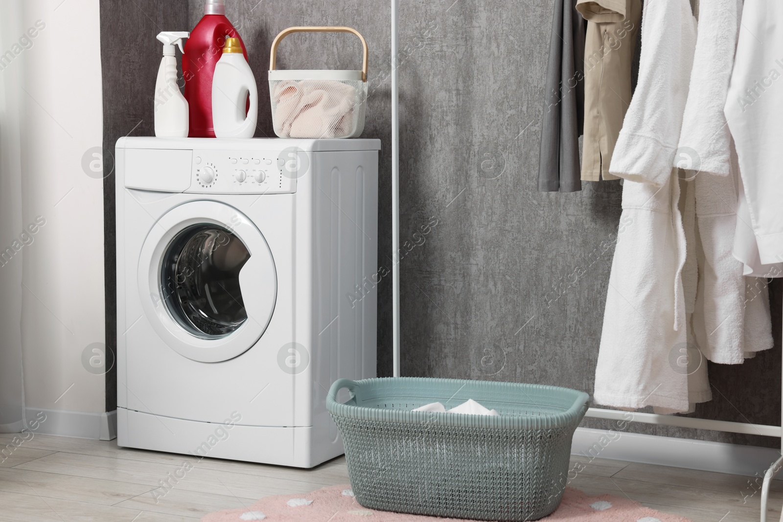 Photo of Washing machine, detergents, baskets and clothing rack indoors