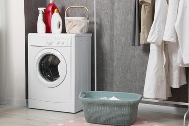 Photo of Washing machine, detergents, baskets and clothing rack indoors