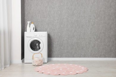 Photo of Washing machine, detergents and basket with laundry near grey wall indoors, space for text