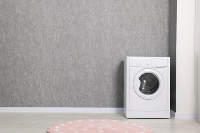 Washing machine near grey wall indoors, space for text