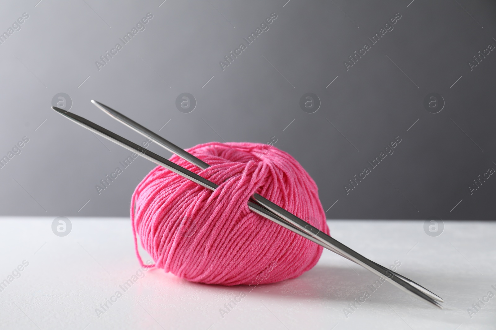 Photo of Pink skein of yarn and knitting needles on white table against grey background