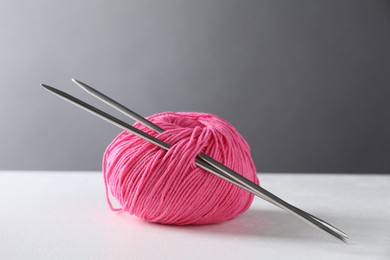 Pink skein of yarn and knitting needles on white table against grey background