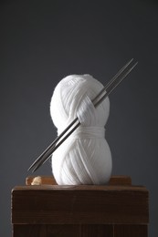 Skein of white yarn and knitting needles on wooden stand against grey background