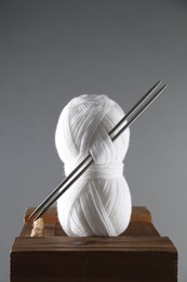 Skein of white yarn and knitting needles on wooden stand against grey background