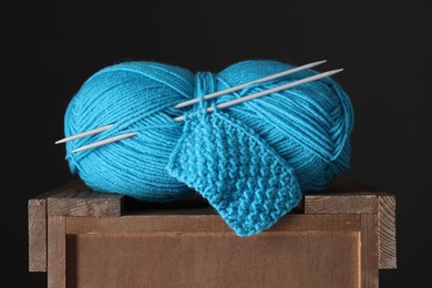 Skein of light blue yarn, knitted fabric and needles on wooden stand