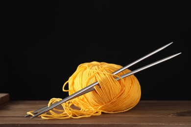 Skein of orange yarn and knitting needles on wooden table