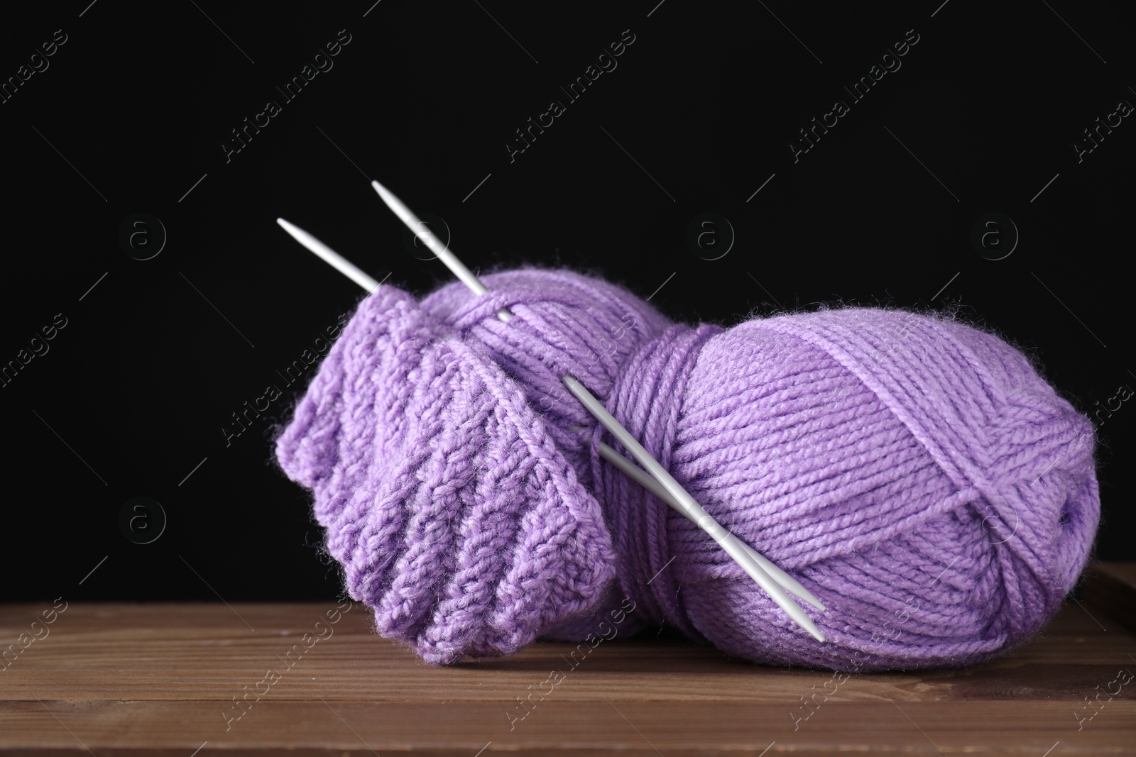 Photo of Skein of violet yarn, knitted fabric and needles on wooden table