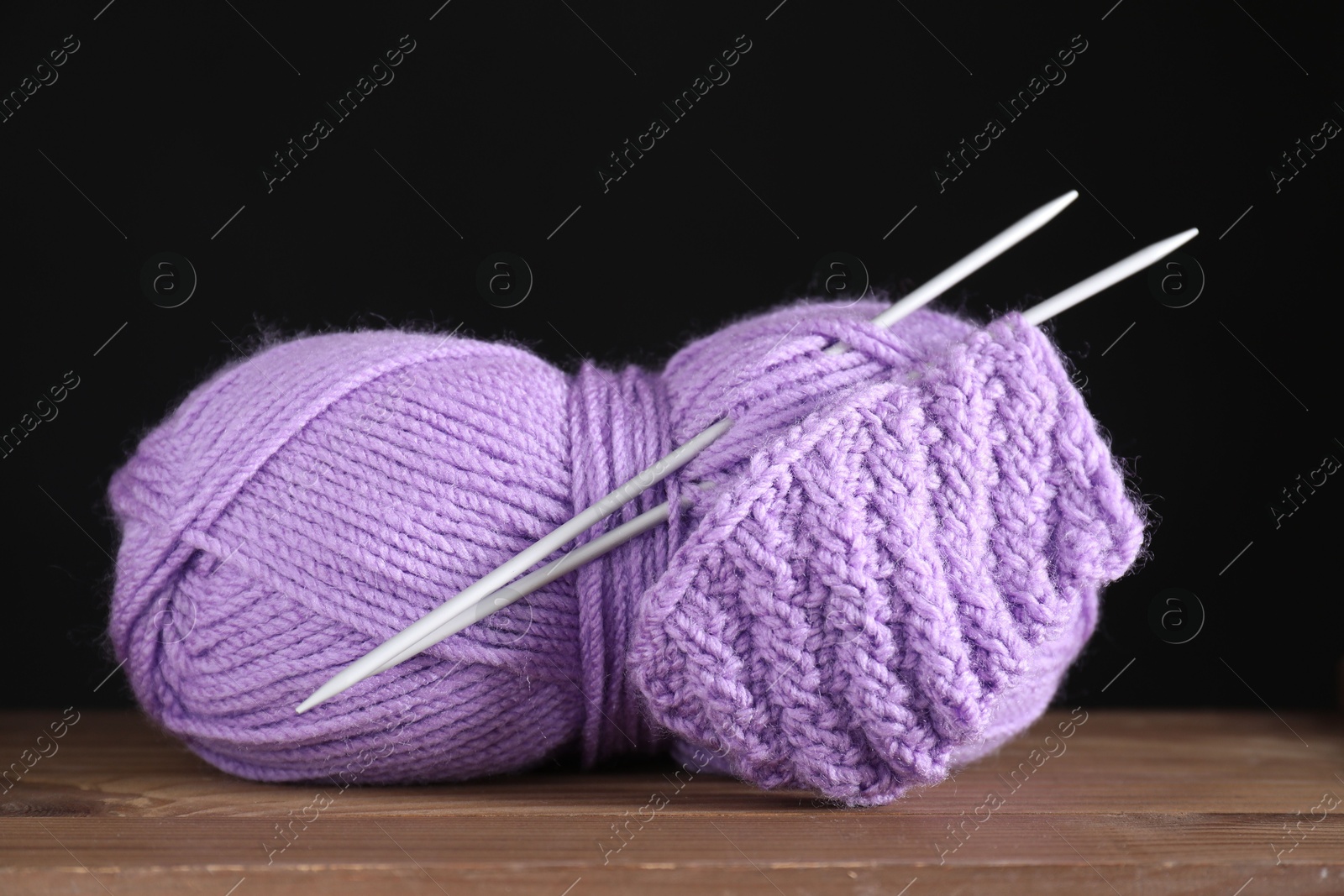 Photo of Skein of violet yarn, knitted fabric and needles on wooden table