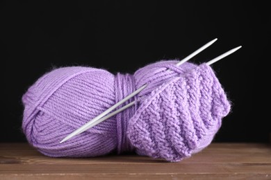 Photo of Skein of violet yarn, knitted fabric and needles on wooden table