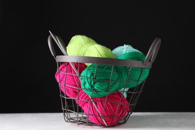 Photo of Many soft skeins of yarn and knitting needles in metal basket on white table